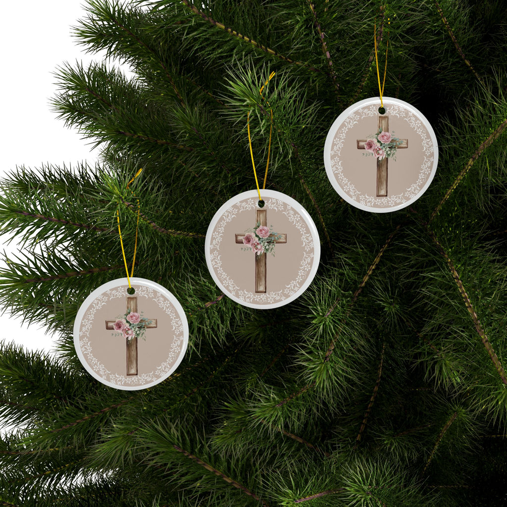 Three round ceramic cross ornaments with pink roses and white lace borders hanging on a tree